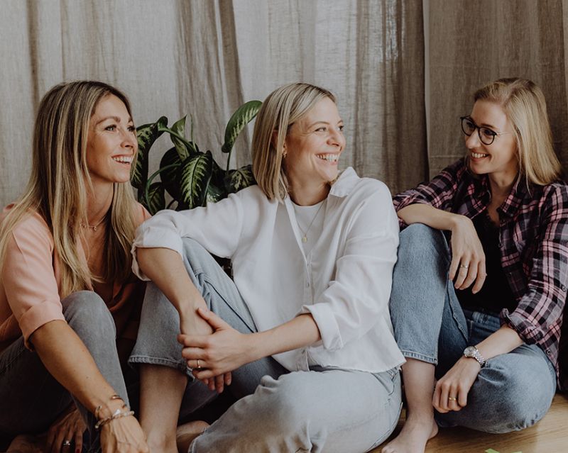 MamAcademy Dr. Rieke Hermann und Team sitzen auf dem Boden und lachen sich an